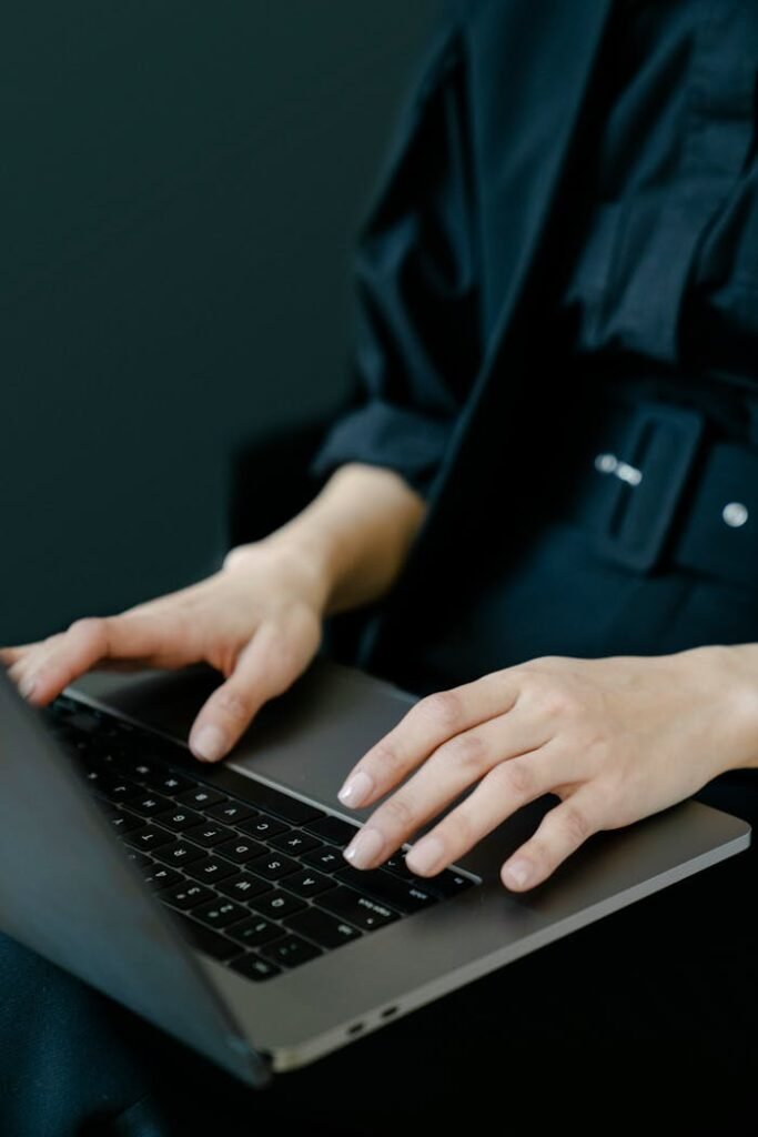 Crop unrecognizable female freelancer in black clothes typing on netbook keyboard while working on project