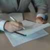 person in gray suit holding white pen and document on a clipboard